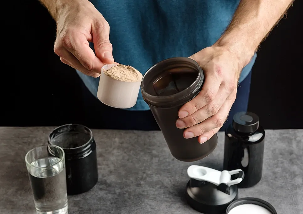 Man scooping protein powder into a shaker bottle