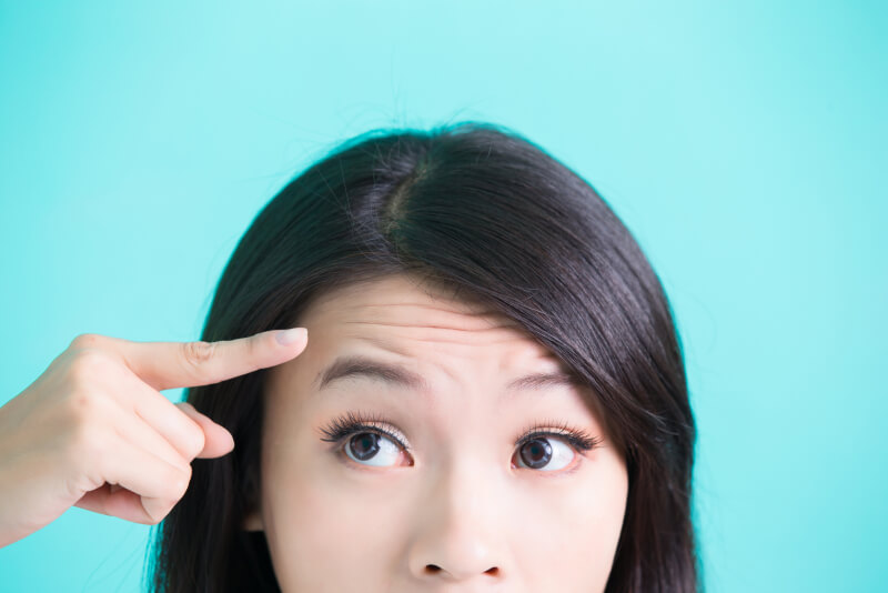 Shot of a woman's face with her finger pointing at her forehead on a blue background