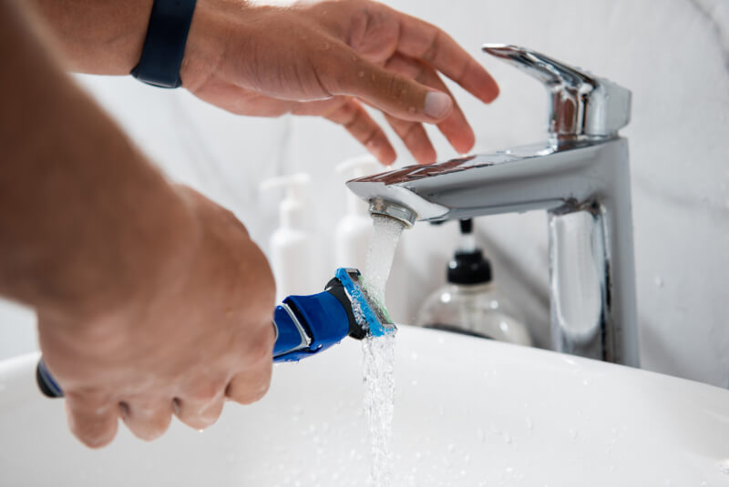 Close up portrait of young male hands washing razor under tap water in bathroom