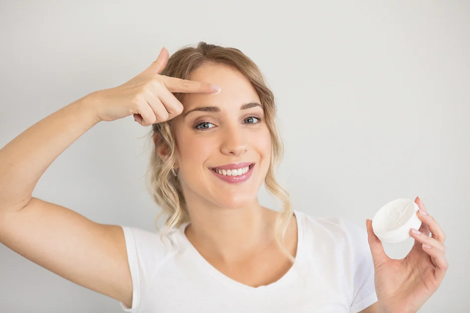 smiling woman applies moisturizer on her forehead