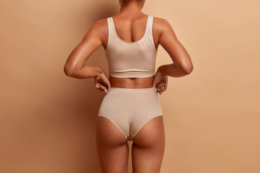 slim woman poses in panties and top has perfect figure healthy dark skin isolated on brown background